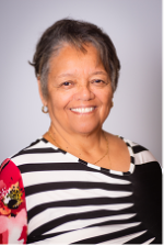 A person with gray hair and smiling. They are wearing hoop earrings and a black and white striped shirt with a red sleeve.