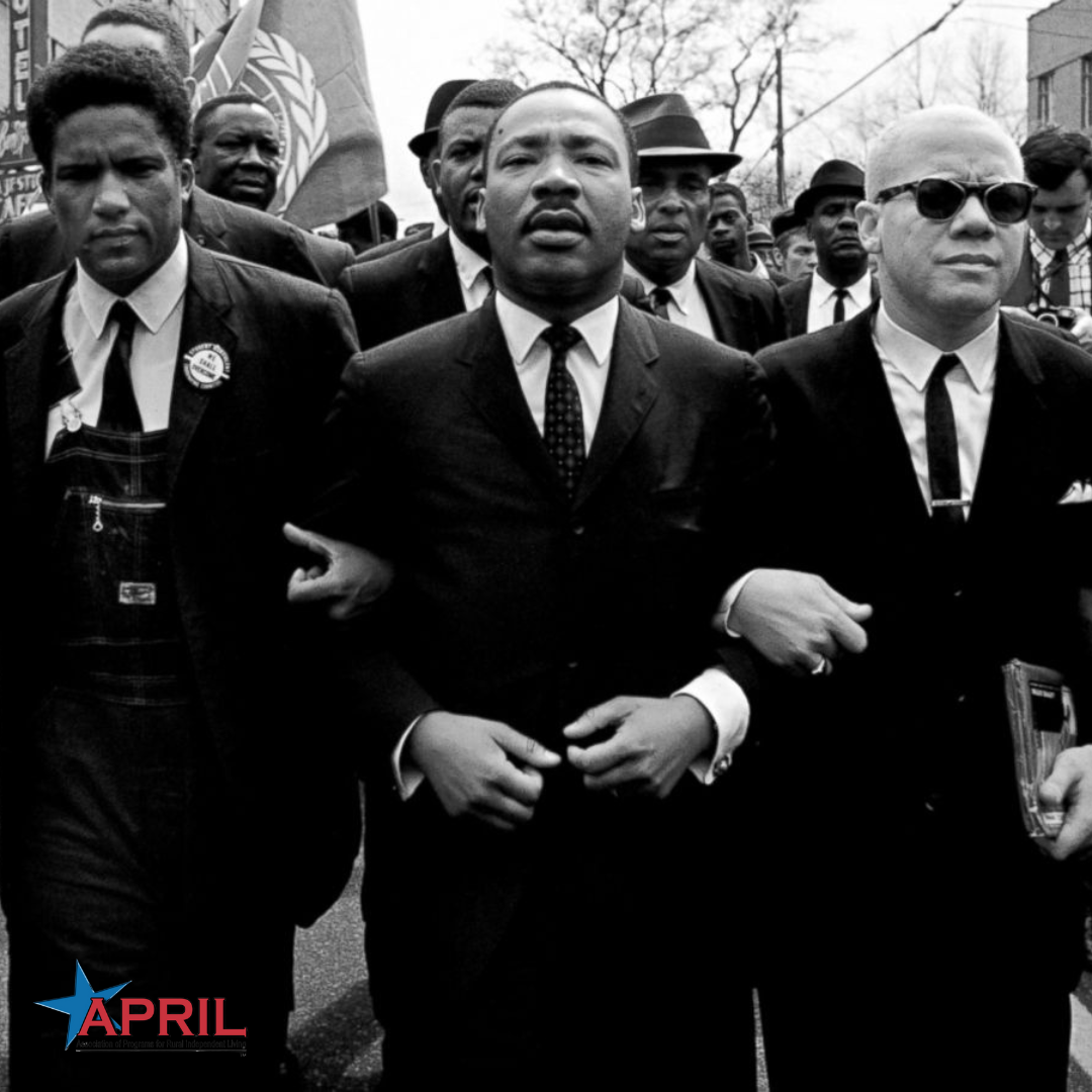 Black and white photo of Martin Luther King, Jr. with other civil rights leaders walking arm-in-arm down a street with followers behind them. APRIL logo is in the bottom left corner.