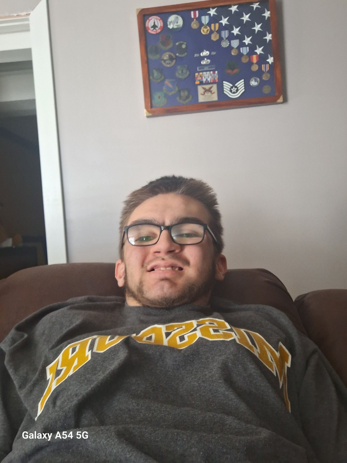 Photo of Zach Cox, a young white male with shorter dark hair and dark rimmed glasses. He is sitting on a couch wearing a sweatshirt.